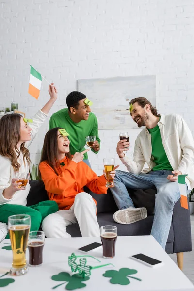 Amazed woman pointing at bearded friend with sticky note on forehead while playing guess who game on Saint Patrick Day — Fotografia de Stock