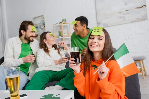 Щаслива жінка з королівським словом на липкій ноті з ірландським прапором і склянкою пива біля міжрасових друзів у День Святого Патрика. — стокове фото