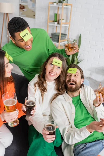 Cheerful interracial friends with drinks playing who i am game at home — Stock Photo