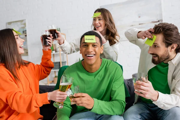 Smiling african american man holding whiskey while playing who i am game with friends at home — Stock Photo