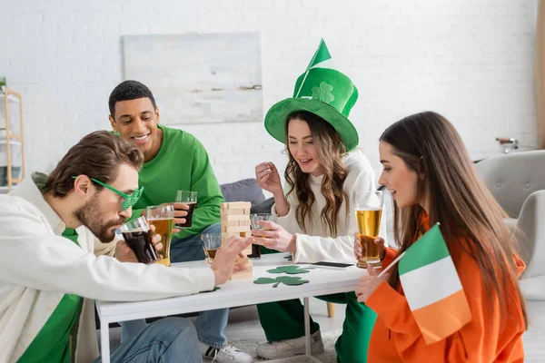 Multiethnic friends celebrating saint patrick day and playing wood blocks game at home — Stock Photo