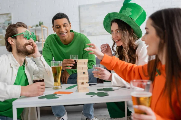 Amigos multiétnicos positivos com cerveja jogando jogo de blocos de madeira enquanto celebra o dia de São Patrício — Fotografia de Stock