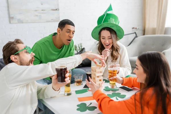 Des amis multiethniques excités avec de la bière jouant au jeu des blocs de bois le jour de la Saint Patrick — Photo de stock