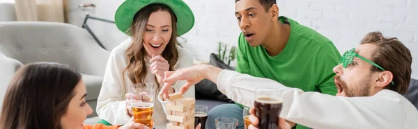 Des amis multiethniques excités avec de la bière jouant au jeu des blocs de bois à la maison, bannière — Photo de stock