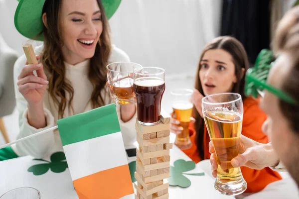 Glass of beer on wood blocks game near blurred friends celebrating saint patrick day at home — Photo de stock