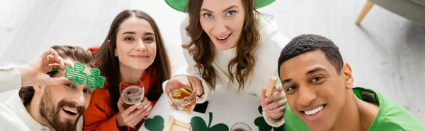 Overhead view of cheerful interracial friends with beer celebrating saint patrick day at home, banner — Stock Photo