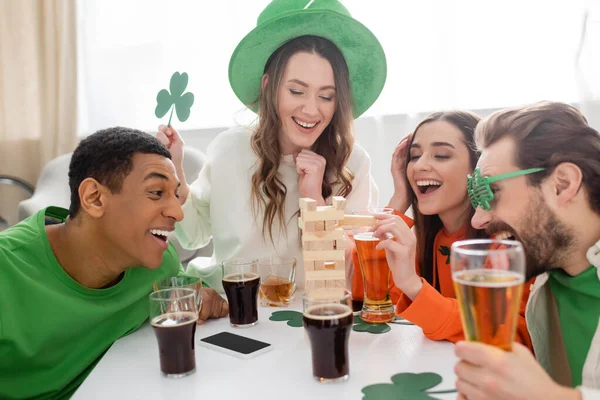 Positive multiethnic friends with beer playing wood blocks game during saint patrick day — Stock Photo