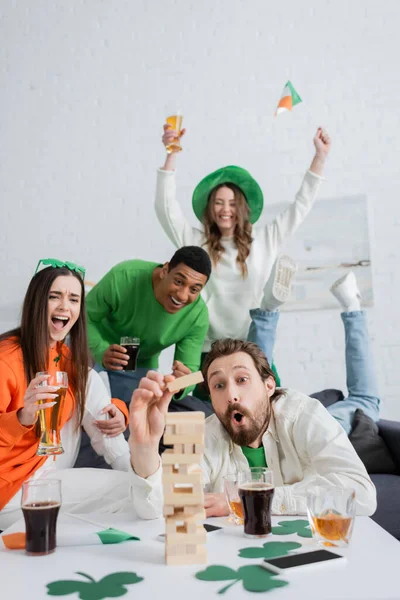 Aufgeregte interrassische Freunde beim Holzklötzchenspiel bei Bier und Whisky zu Hause — Stockfoto