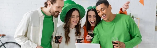 Багатоетнічні друзі з пивом, використовуючи цифровий планшет під час святого патрульного дня вдома, банер — стокове фото