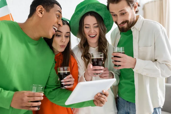 Africano americano segurando tablet digital perto de amigos com cerveja durante o dia de santo patrick em casa — Fotografia de Stock