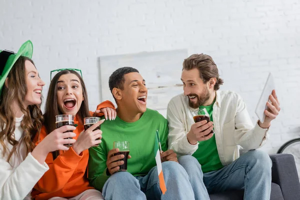 Amigos multiétnicos entusiasmados com cerveja e tablet digital celebrando o dia de São Patrício em casa — Fotografia de Stock