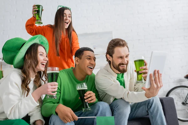 Багатоетнічні друзі з зеленим пивом, використовуючи цифровий планшет на день святого патруля — стокове фото