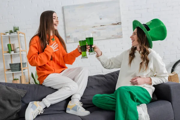 Joyeux jeunes femmes cliquetis bière verte et parler sur le canapé le jour de saint Patrick — Photo de stock