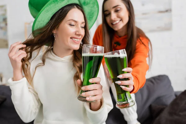 Smiling blurred women clinking green beer during saint patrick celebration at home — Stock Photo