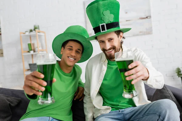 Interracial men in green hats holding beer during saint patrick day — Stock Photo