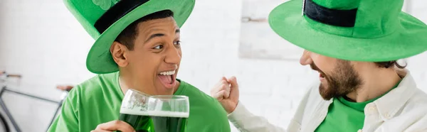 Excited multiethnic men with green beer celebrating saint patrick day at home, banner — Stock Photo
