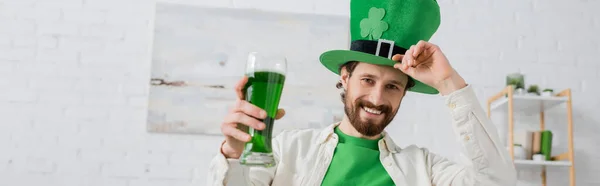Позитивный человек держит зеленое пиво и шляпу в день святого Патрика дома, баннер — стоковое фото