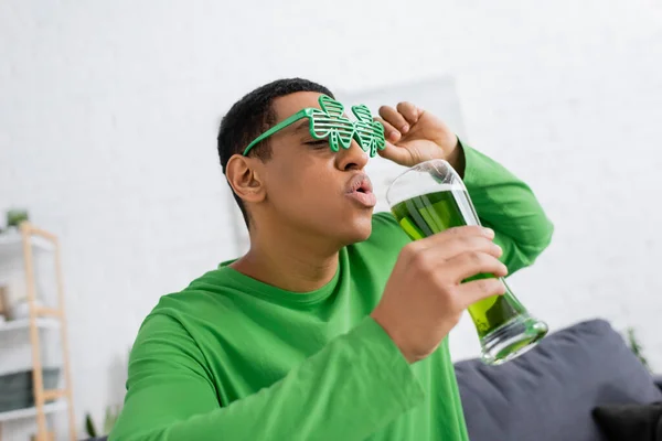 Africano americano em óculos de sol de festa segurando cerveja verde durante o dia de santo patrick — Fotografia de Stock