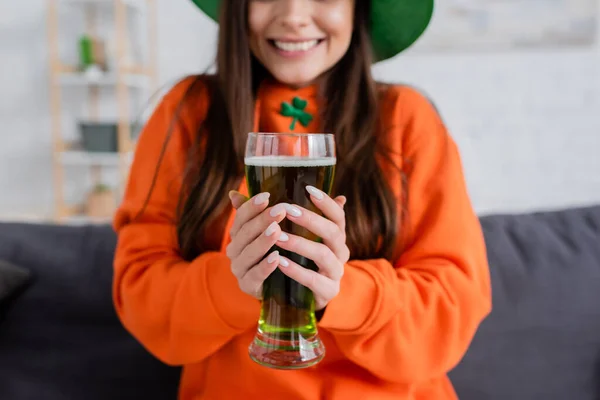 Vista recortada de una mujer borrosa sosteniendo un vaso de cerveza verde durante el día de San Patricio - foto de stock