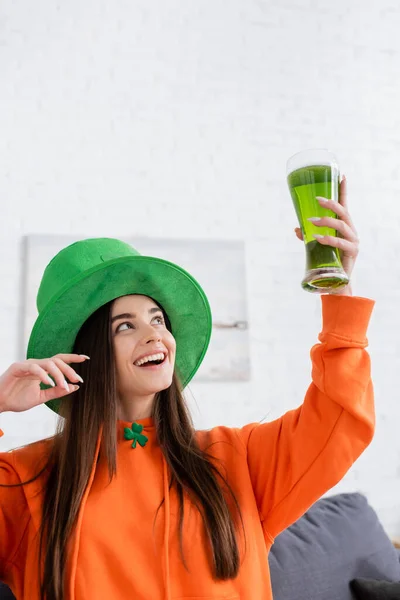 Mujer alegre en sombrero verde sosteniendo vaso de remolacha en la sala de estar - foto de stock