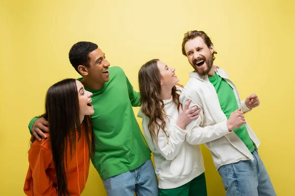 Cheerful interracial friends looking at man on yellow background — Stock Photo