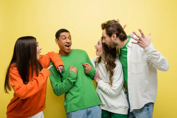 Amazed friends looking at african american man on yellow background — Stock Photo