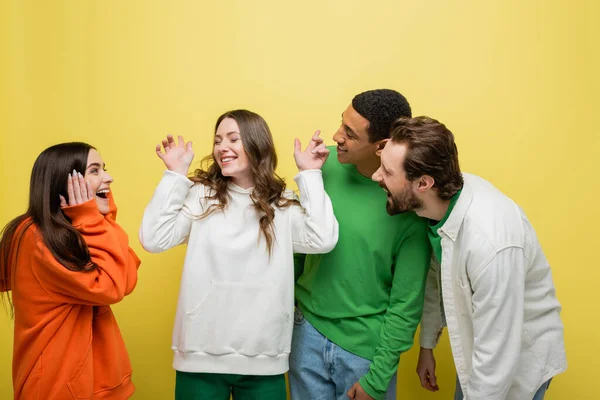 Smiling interracial people looking at friend on yellow background — Stock Photo