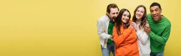 Multiethnic friends in casual clothes looking at camera isolated on yellow, banner — Stock Photo