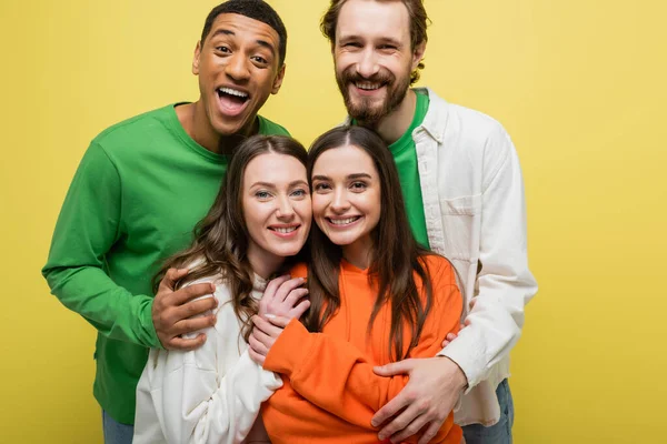 Cheerful interracial men hugging friends isolated on yellow — Stock Photo