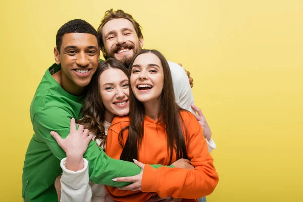 Lächelnde multiethnische Freunde, die sich isoliert auf gelb umarmen — Stockfoto