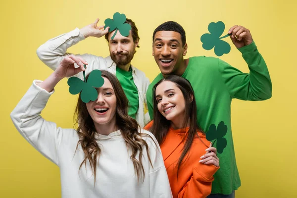 Smiling multiethnic friends having fun with paper clover isolated on yellow — Stock Photo