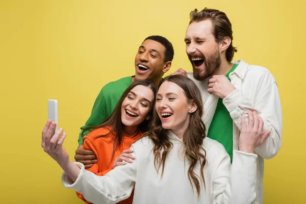 Positive multiethnic friends using mobile phone isolated on yellow — Stock Photo