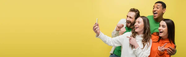Multiethnic friends using cellphone and gesturing isolated on yellow, banner — Stock Photo