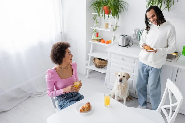 High angle view of positive african american couple holding breakfast near labrador in kitchen - foto de stock