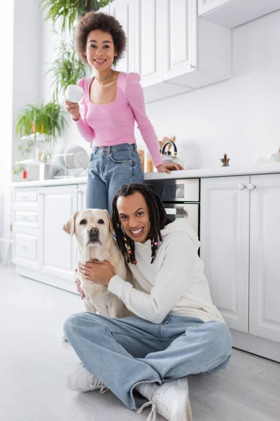 Positiva pareja afroamericana con café y labrador mirando a cámara en cocina - foto de stock