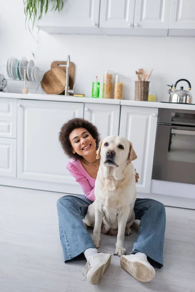 Femme afro-américaine positive regardant labrador dans la cuisine — Photo de stock