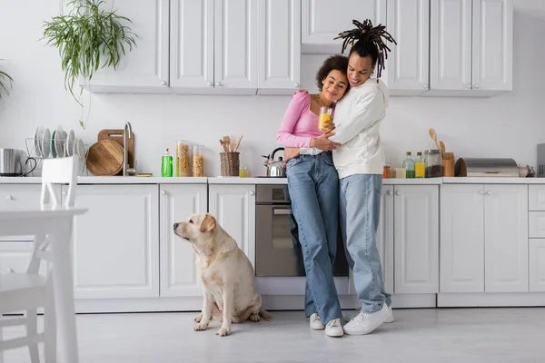Cheerful african american couple hugging near labrador in kitchen — Foto stock