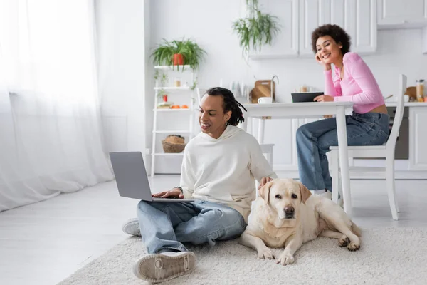 Labrador lying near african american freelancers in kitchen — Stock Photo