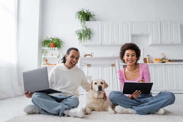 Positive african american couple of freelancers looking at camera near labrador at home — Stock Photo