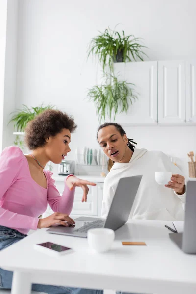 African american freelancer pointing at laptop near boyfriend with coffee in kitchen — Photo de stock
