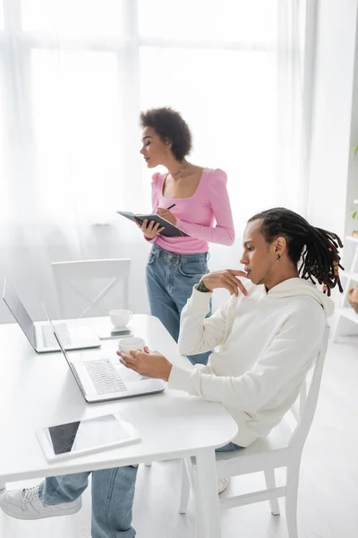 Vista lateral de freelancers afroamericanos usando aparatos cerca del café en casa - foto de stock