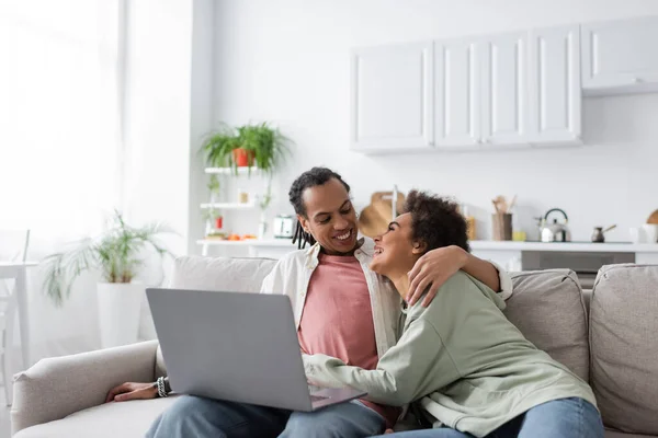 Souriant couple afro-américain étreignant et se regardant près d'un ordinateur portable — Photo de stock