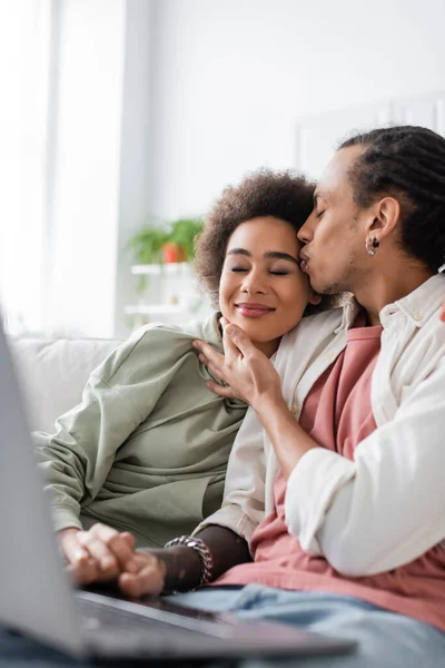 Coppia afroamericana che si tiene per mano vicino al computer portatile offuscato sul divano — Foto stock