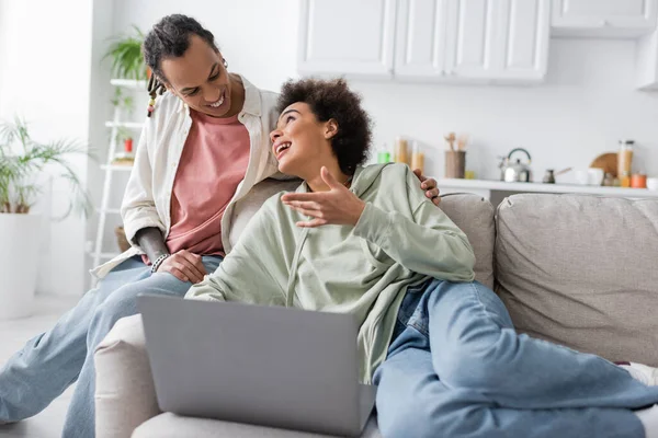 Young african american woman talking to smiling boyfriend near laptop on couch — Photo de stock