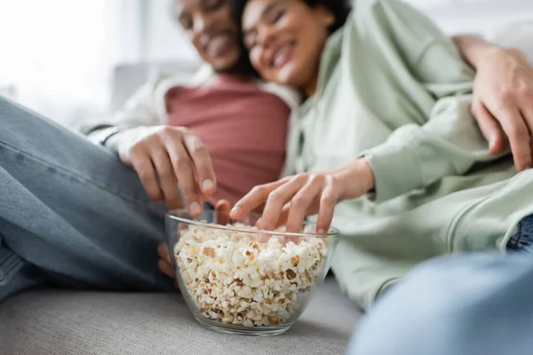 Popcorn near blurred african american couple resting on couch — Stock Photo