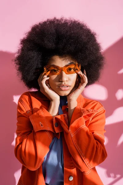 Giovane donna afroamericana in elegante occhiali da sole arancioni e abito alla moda in posa su rosa — Foto stock