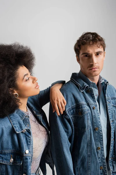 Curly african american woman leaning on shoulder of young man in denim outfit isolated on grey — Stockfoto