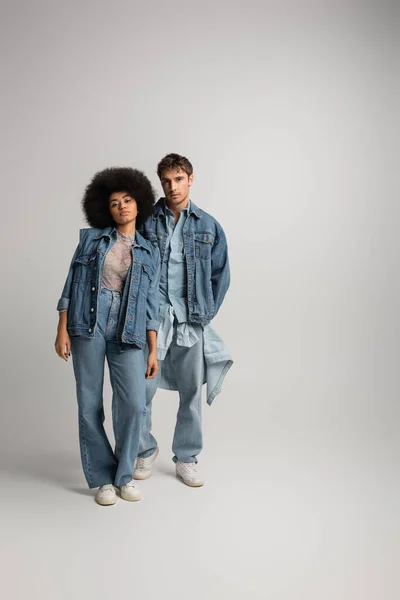 Full length of young interracial man and woman standing in total denim outfit on grey — Stock Photo