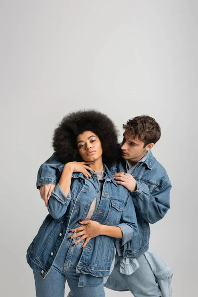 Man in denim jacket embracing curly african american woman isolated on grey — Stock Photo