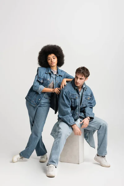 Full length of brunette african american woman in sneakers standing near man in denim outfit on grey — Stock Photo